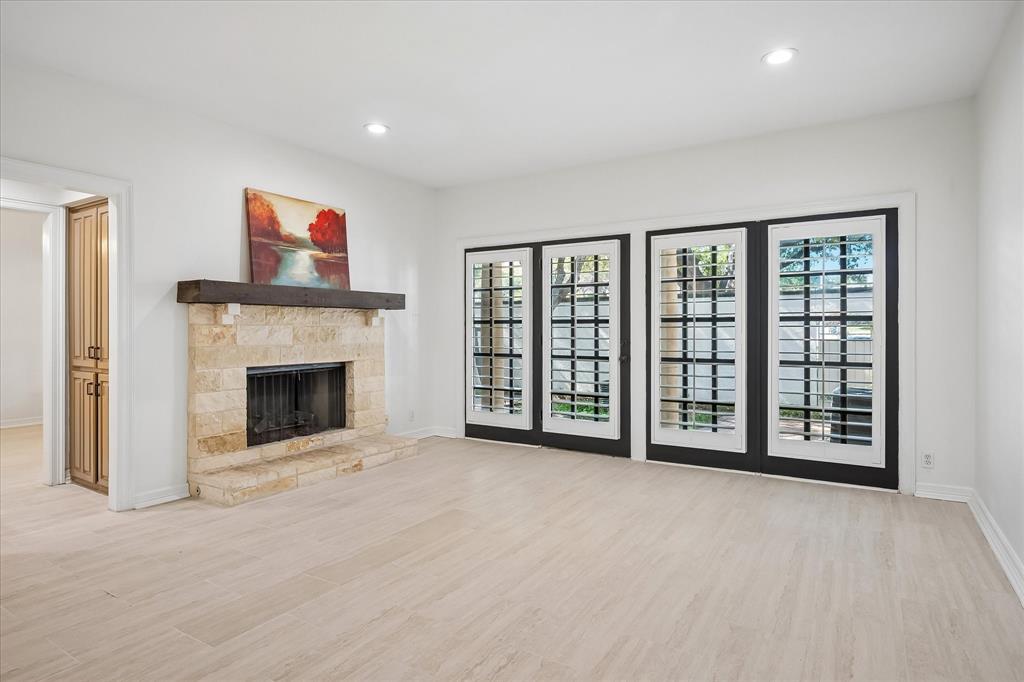 Stone fireplace with a prominent timber mantel, light-toned wood-finish flooring, and multiple sets of glass-paneled doors with black frames