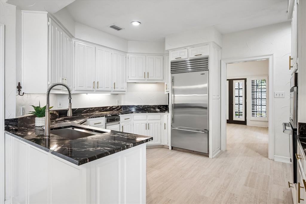 Kitchen featuring white cabinetry, dark stone countertops, integrated stainless steel refrigerator, undermount sink with pull-down faucet, and light-tone flooring