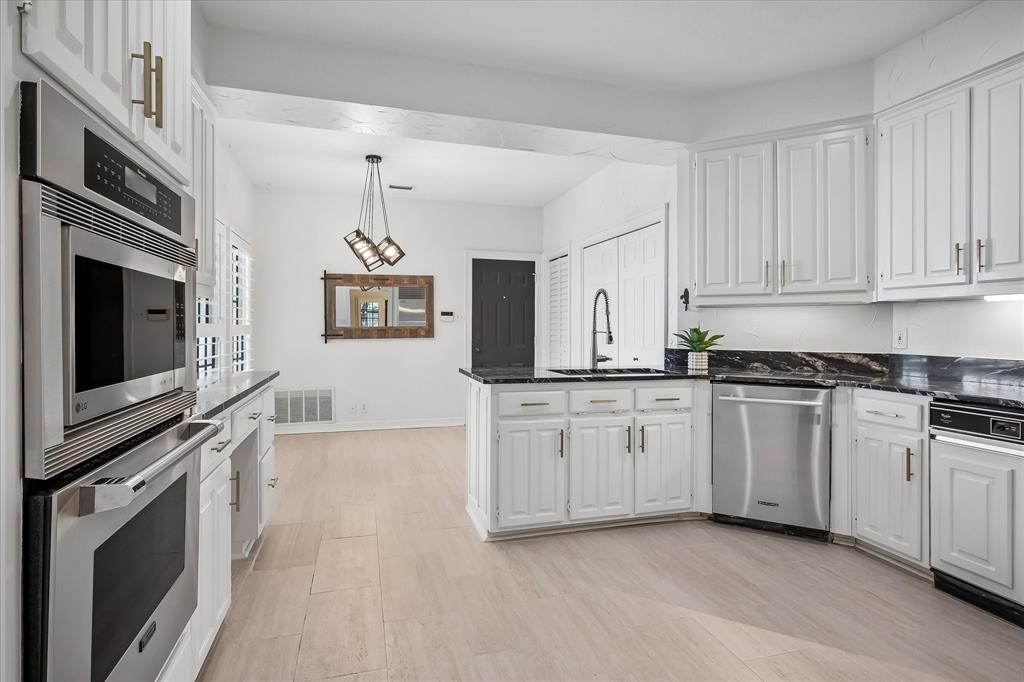 Kitchen featuring white cabinetry with gold-tone hardware, dark stone countertops, stainless steel wall-mounted oven and microwave, and light-toned wood-finish flooring