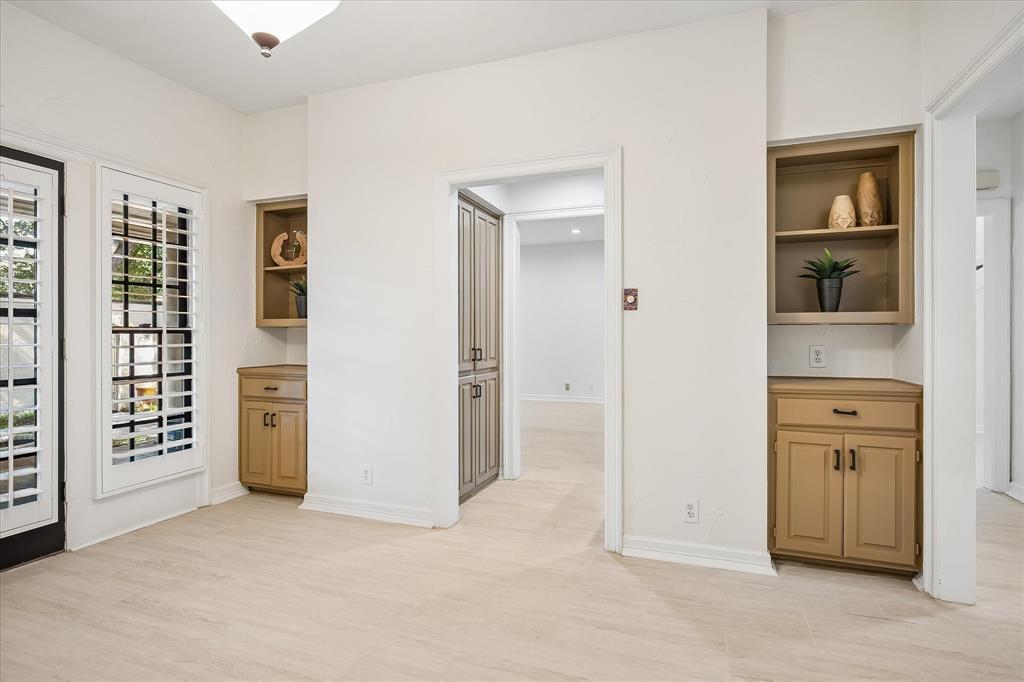 Wood-finish flooring, dual built-in cabinetry units with open shelving, full-height pantry storage, and window shutters