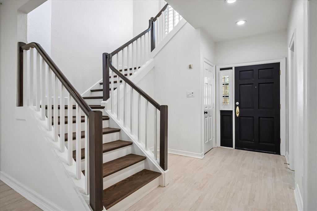 Foyer featuring a black paneled front door with a glass sidelight, wood-finish flooring, and a staircase with white balusters and dark-stained handrails and treads