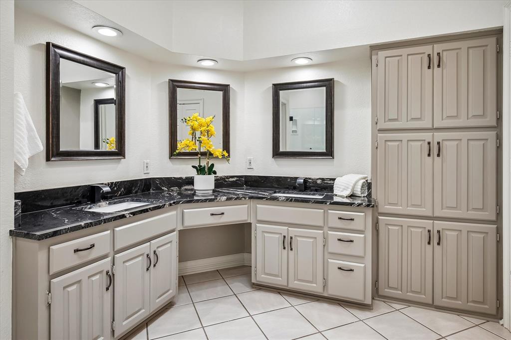 Dual-sink vanity with dark stone countertop, inset rectangular basins, recessed lighting, and extensive built-in floor-to-ceiling cabinetry