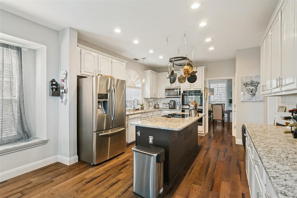 Kitchen featuring wood-finish flooring, white cabinetry, a center island with a stone-finish countertop, stainless steel appliances, and recessed lighting