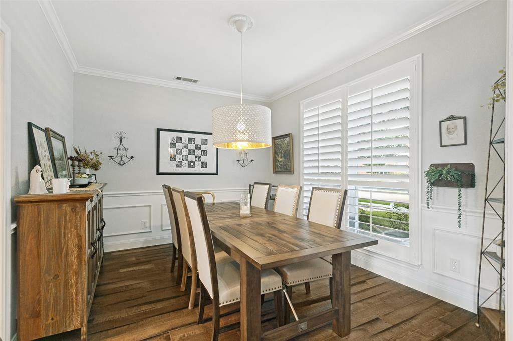 Dining area featuring wood-finish flooring, wainscoting, crown molding, plantation shutters, and a drum pendant light fixture