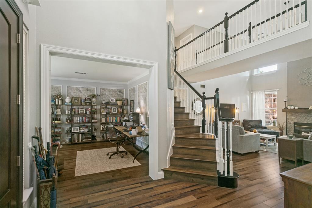 Two-story foyer featuring high ceilings, wood-finish flooring, a wood-tread staircase with white railings, and a stone-surround fireplace