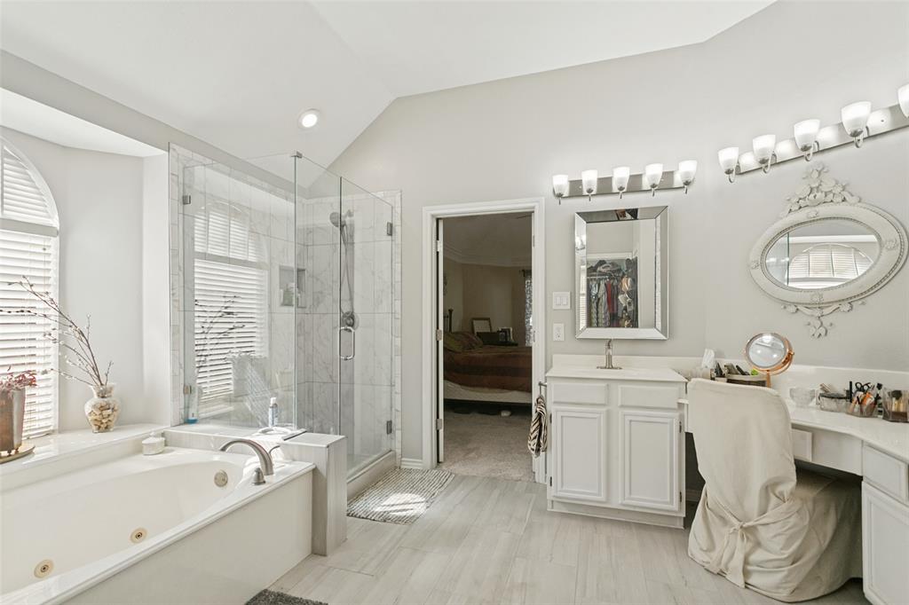 Bathroom featuring a jetted soaking tub, glass-enclosed shower with tiled surround, dual-mirrored vanity area with built-in cabinetry, and wood-finish flooring