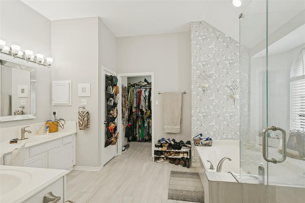 Bathroom featuring a dual-sink vanity with white cabinetry, a glass-enclosed shower, a deep soaking tub, and ceramic tile flooring