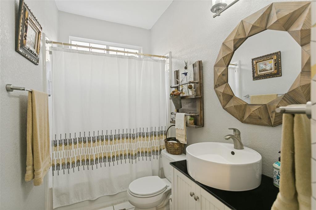 White oval vessel sink with a brushed-finish faucet, dark countertop, white beadboard vanity cabinet, and brushed-finish wall-mounted light fixture
