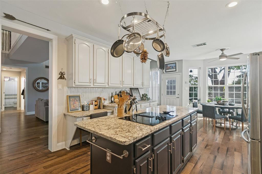 Kitchen featuring stone-topped island with a built-in cooktop, overhead pot rack, white cabinetry, and wood-finish flooring