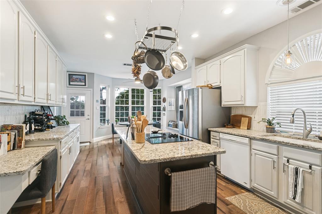 Kitchen featuring white shaker-style cabinetry, stone-finish countertops, a dark-toned center island with an integrated cooktop, recessed lighting, and wood-finish flooring