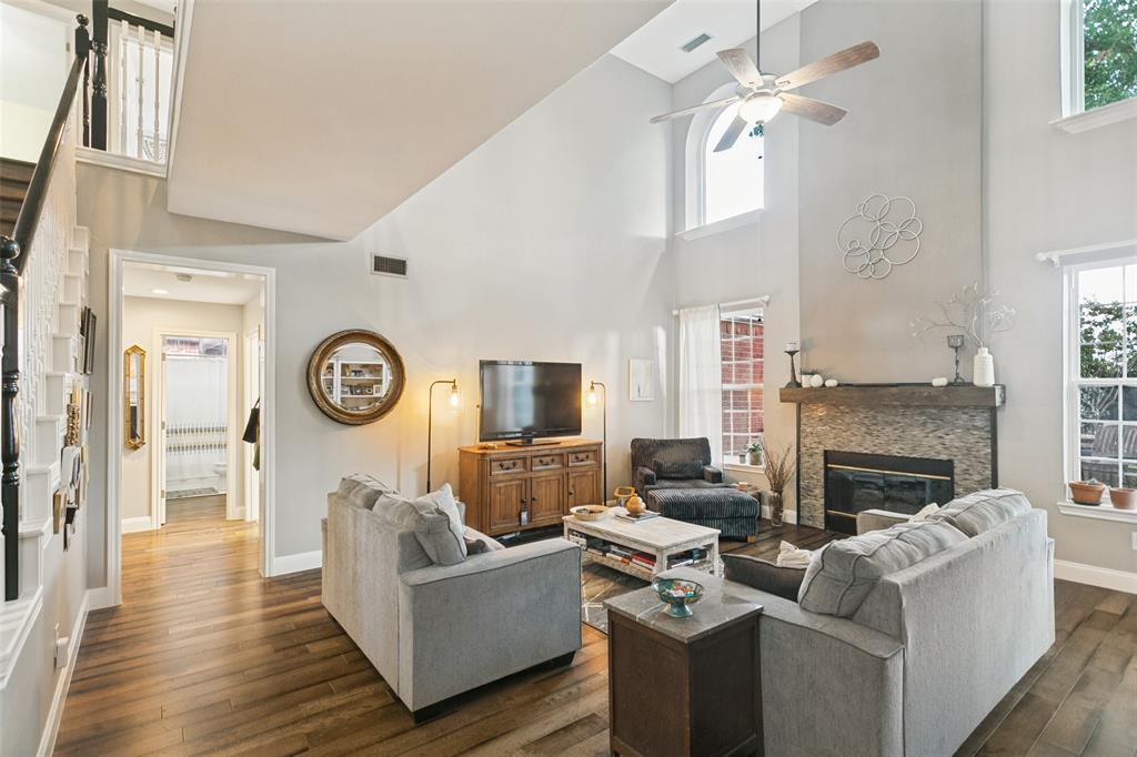 Living area featuring tall ceilings, a floor-to-ceiling fireplace with stone tile surround, wood-finish flooring, and arched windows