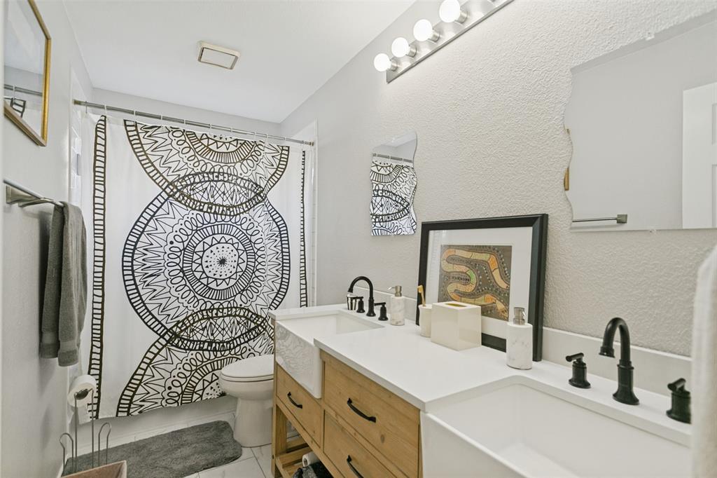 Bathroom featuring a custom wood-finish vanity with dual farmhouse sinks, light-toned countertop, matte black fixtures, and a multi-bulb vanity light
