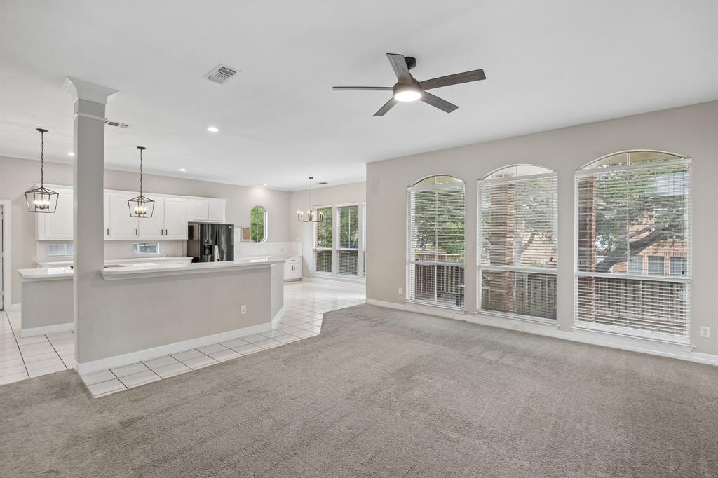 Open-concept interior featuring a peninsula with a breakfast bar, white cabinetry, neutral carpet flooring, a central ceiling fan with an integrated light fixture, and triple arched windows