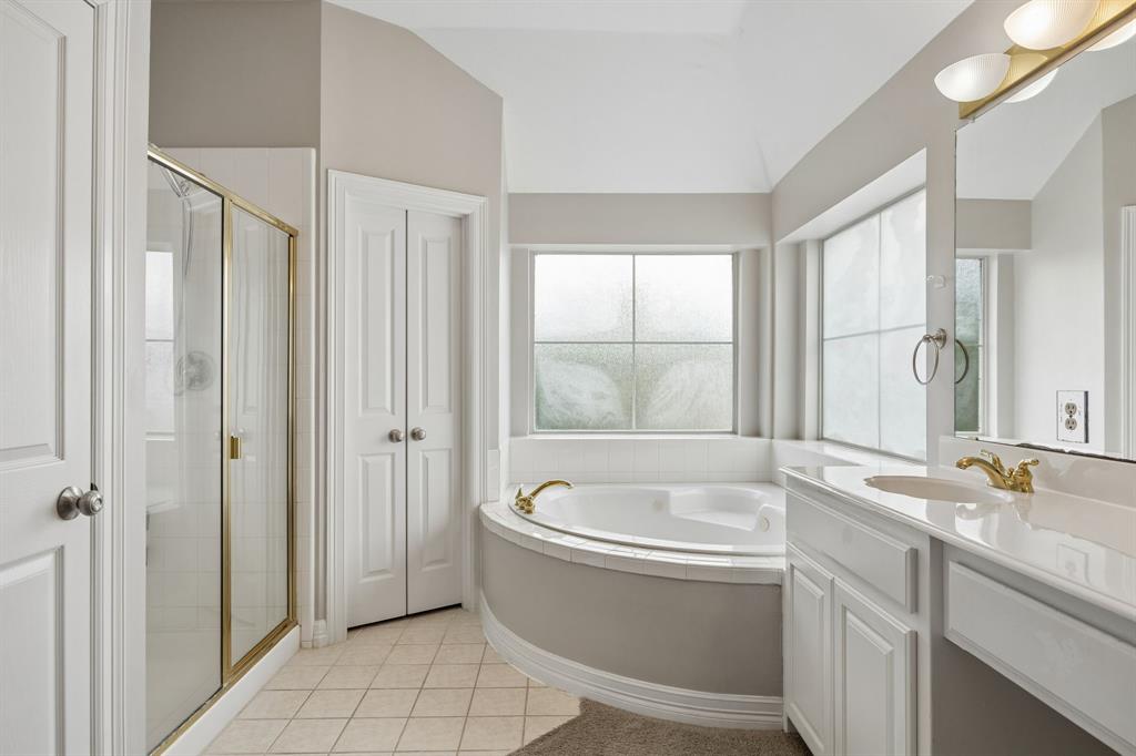 Bathroom featuring a corner soaking tub with tiled surround, separate glass-enclosed shower, dual-sink vanity with white cabinetry, and multi-light wall fixture