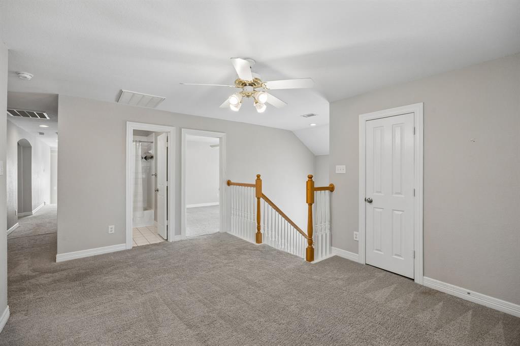 Neutral-toned carpeting, ceiling fan with integrated light fixture, and wooden staircase railing featuring white balusters