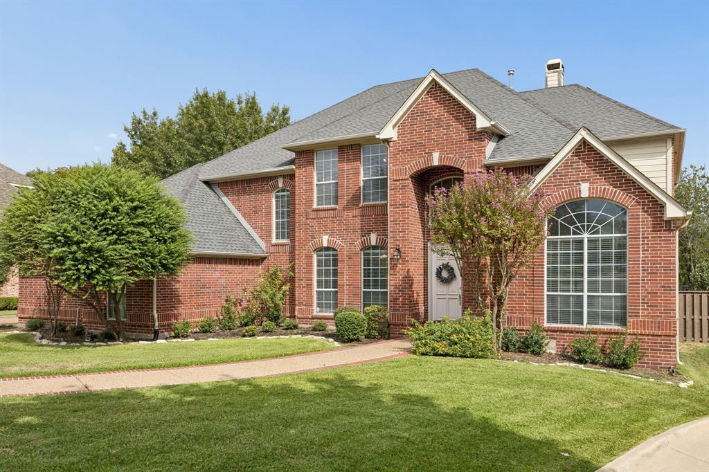 Traditional brick exterior featuring a multi-gabled roofline, arched window detailing, and a manicured front lawn