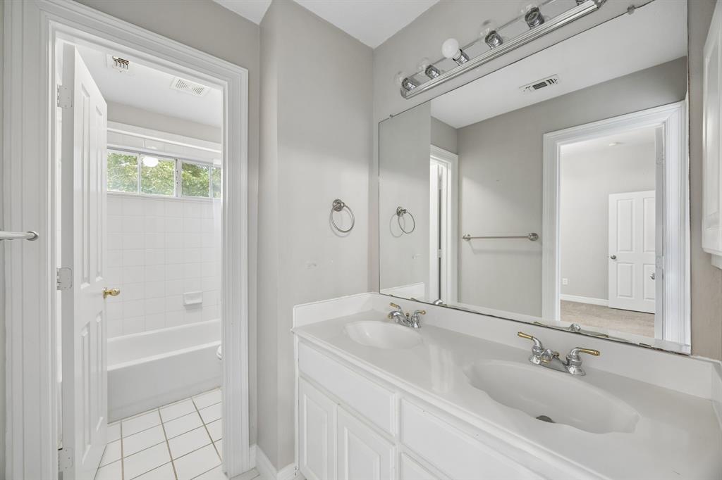 Dual-sink vanity with a solid-surface countertop, full-width wall mirror, brushed nickel plumbing fixtures, and a tiled tub-shower enclosure