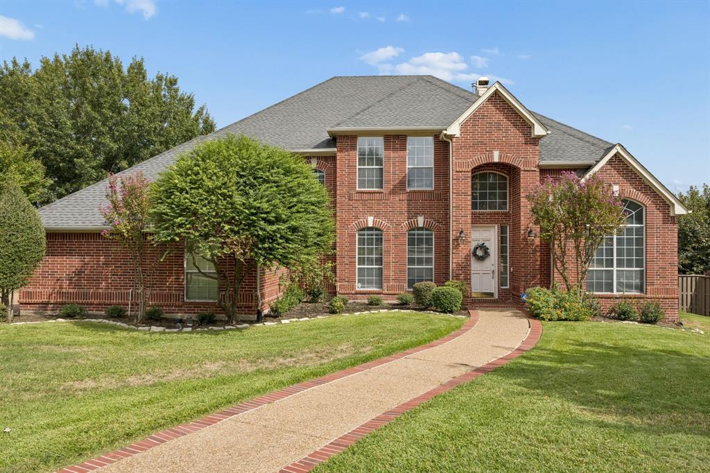Two-story brick exterior featuring a multi-gabled roofline, an arched entryway, stone-texture walkway, and multi-pane windows