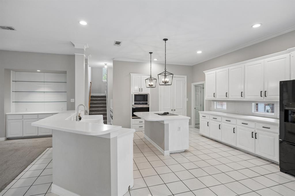 Kitchen featuring white cabinetry, center island with cooktop, built-in wall oven and microwave, ceramic tile flooring, and lantern-style pendant lighting