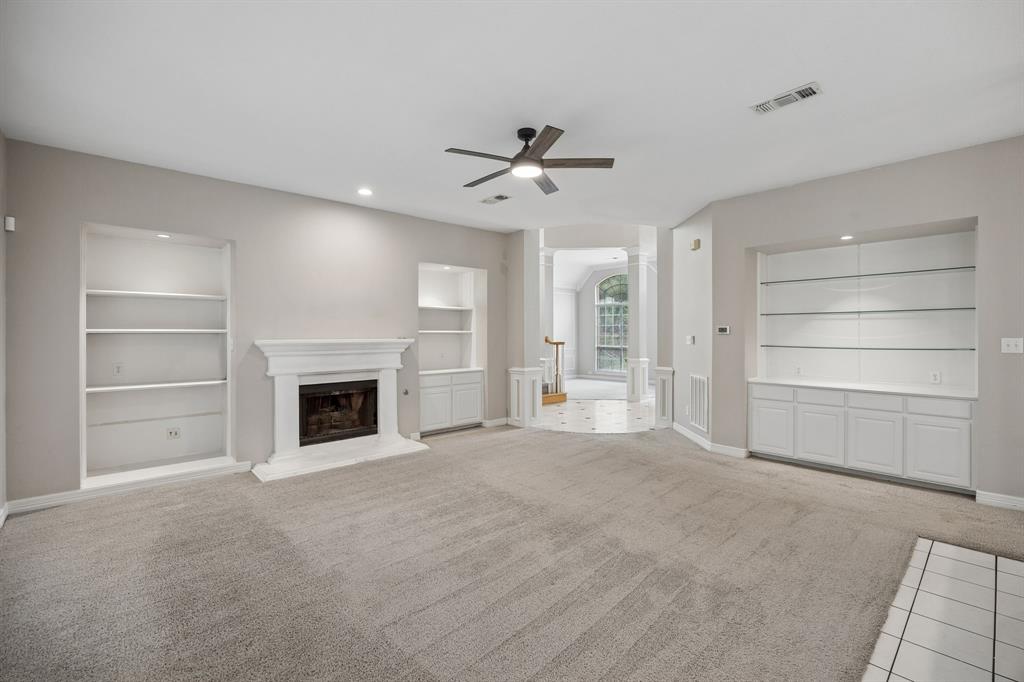 Living room featuring a fireplace with a decorative mantle, three built-in shelving units with lower cabinetry, and a ceiling fan