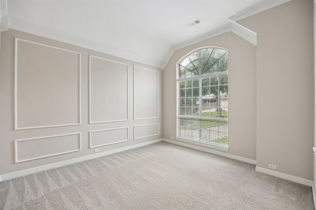 Room featuring vaulted ceilings, arched window with a grid pattern, and walls finished with decorative crown molding and wainscoting panels