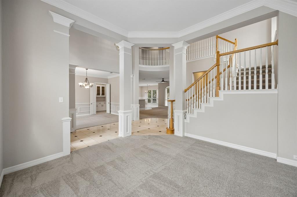 Double-height foyer featuring decorative columns, an open staircase with a wooden handrail, crown molding, and tiled flooring with inset accents