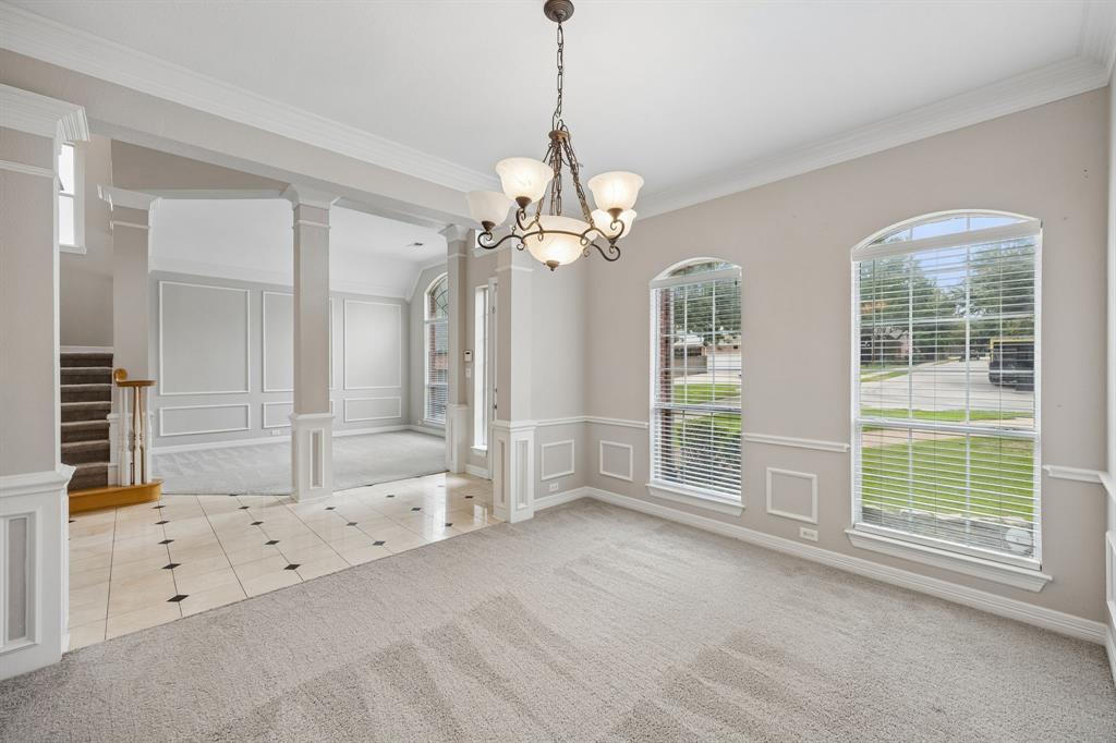 Interior area featuring arched windows, extensive wainscoting, crown molding, multi-toned tile flooring, and a multi-arm chandelier