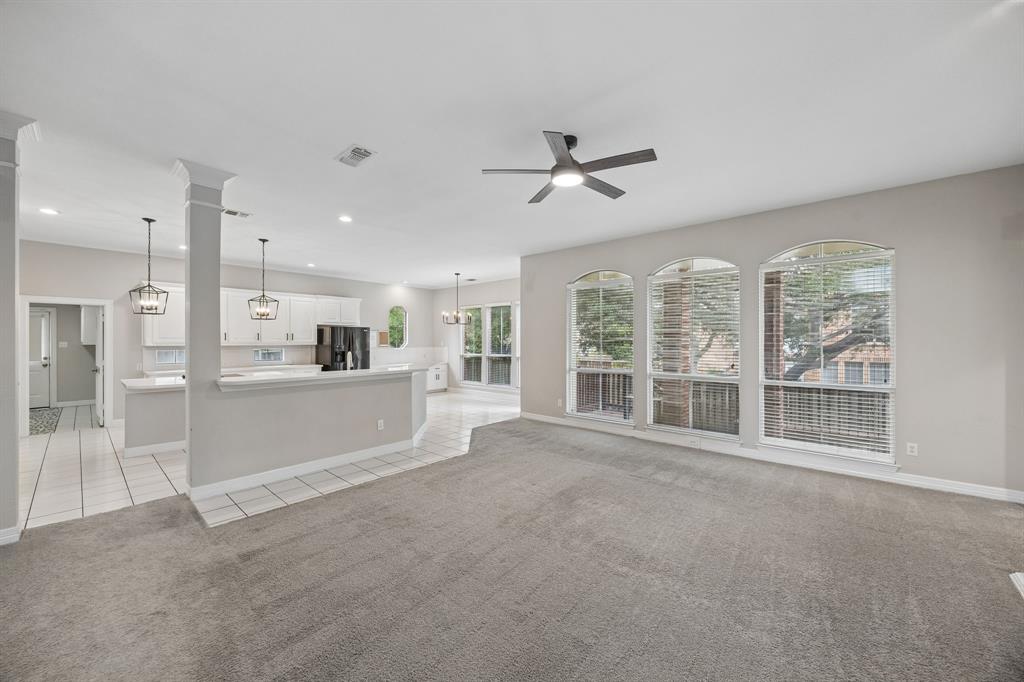 Open-concept interior featuring arched windows, white cabinetry with breakfast bar, neutral carpeting, and a ceiling-mounted fan with integrated light