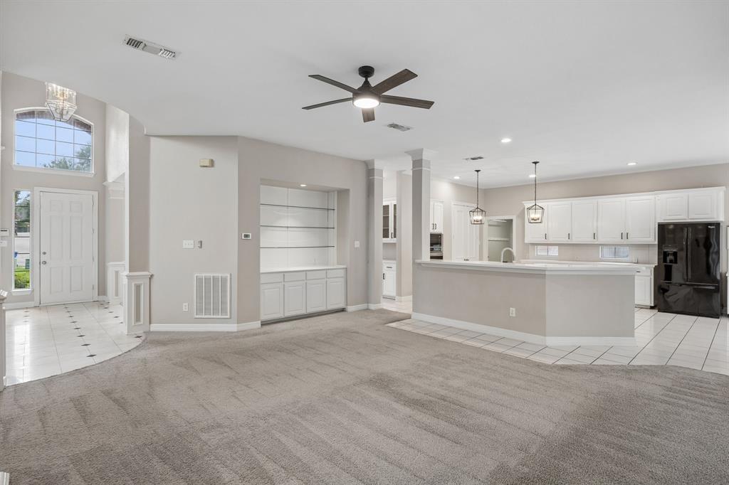 Open-concept interior featuring a breakfast bar, white cabinetry, built-in display shelving, tile flooring, and vaulted ceilings
