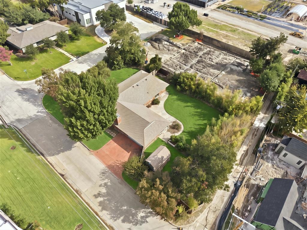 Corner lot featuring a red brick driveway, manicured landscaping, mature trees, and a private rear yard with perimeter bamboo screening