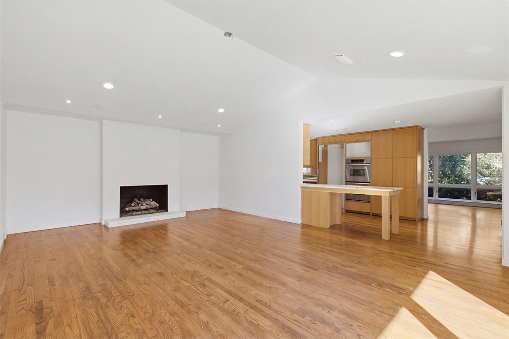 Open living area featuring vaulted ceilings, wood-finish flooring, a recessed fireplace, recessed lighting, and built-in cabinetry with stainless steel wall ovens