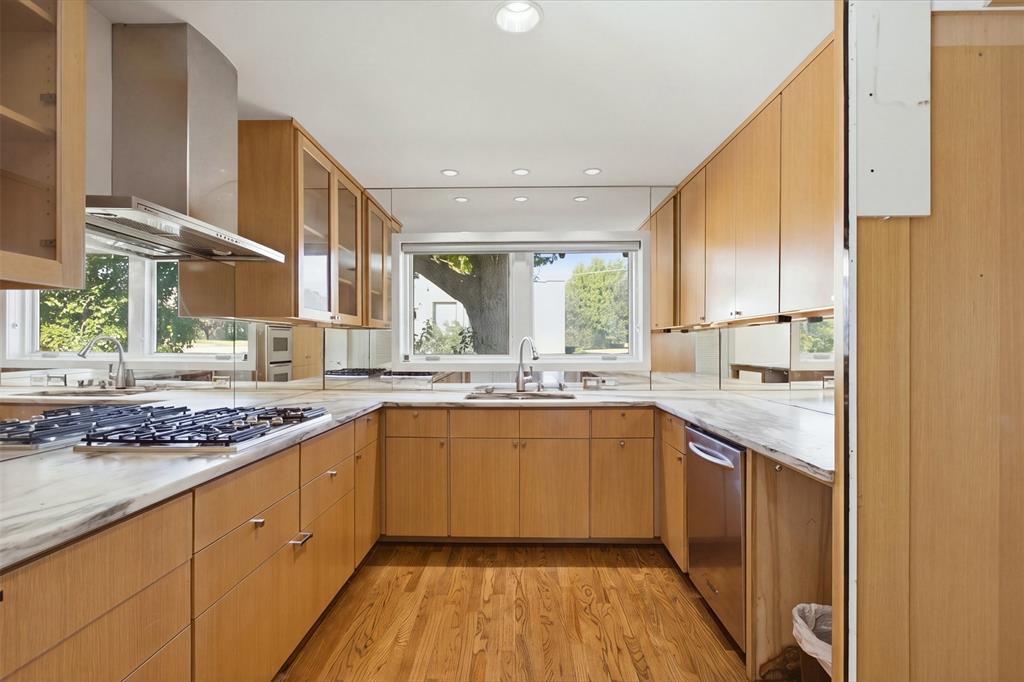Kitchen featuring natural wood-finish cabinetry, stone-surface countertops, a stainless steel gas cooktop with a matching range hood, and wood-finish flooring