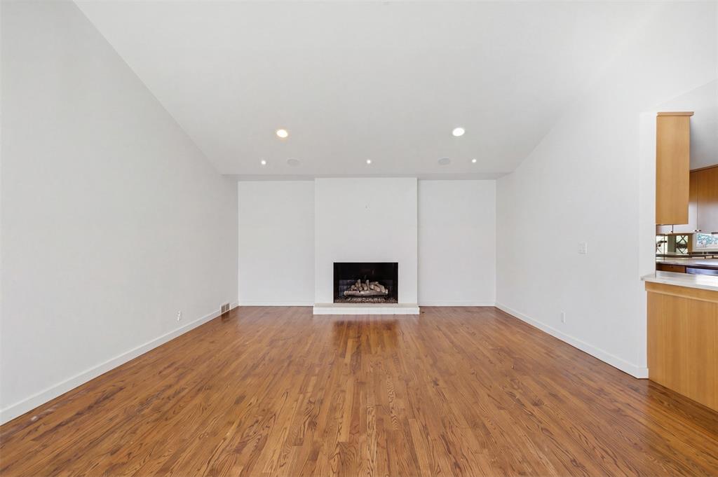 Vaulted ceilings with recessed lighting, wood-finish flooring, and a central fireplace with a raised hearth