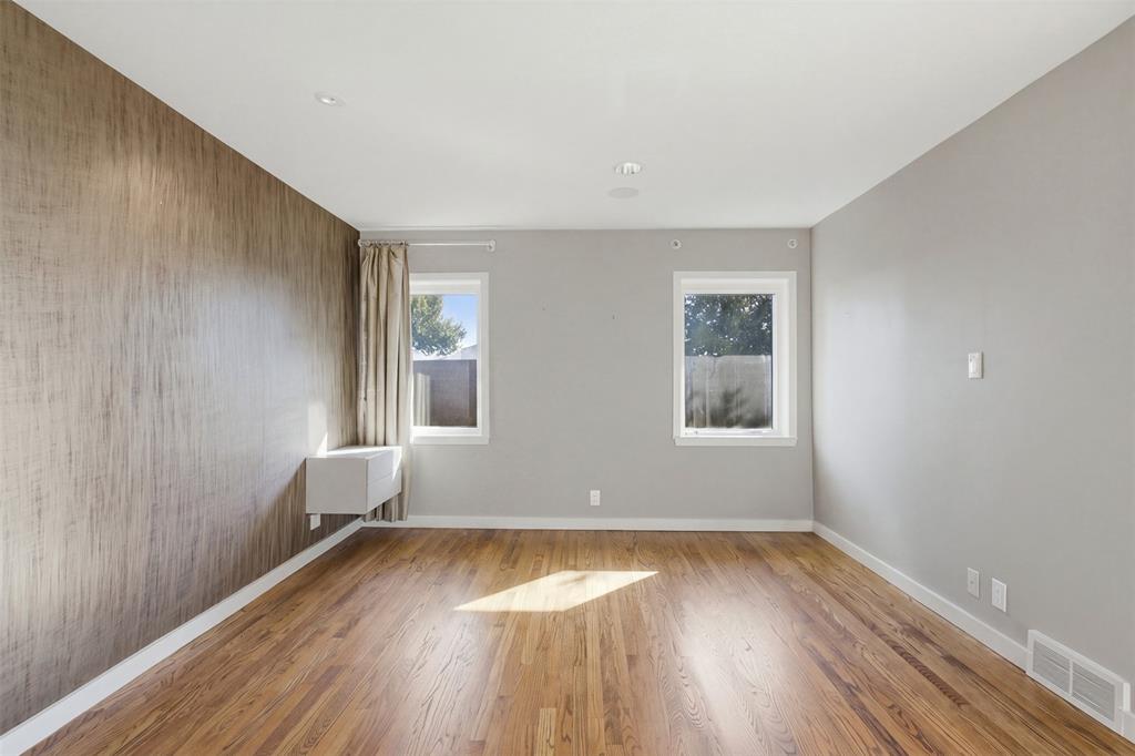 Room featuring wood-finish flooring, a textured accent wall, recessed ceiling lighting, and two windows