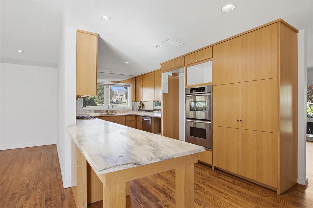 Kitchen featuring flat-panel wood cabinetry, natural stone countertop island, stainless steel double wall ovens, wood-finish flooring, and recessed ceiling lighting