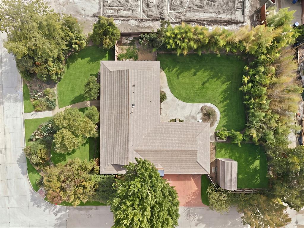 Aerial perspective of a property featuring extensive green space, mature landscaping, a concrete patio, a dedicated storage structure, and a paved driveway