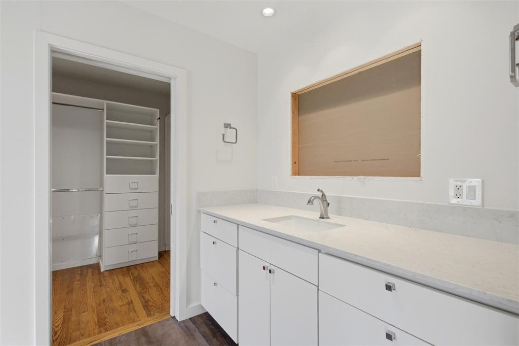 White vanity featuring stone-surface countertop with undermount sink and matte hardware, complemented by custom built-in closet shelving and wood-finish flooring