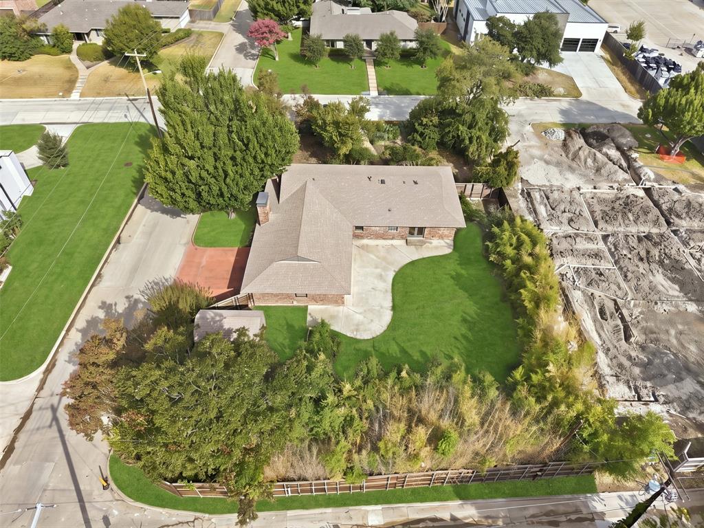 Aerial perspective of a single-story brick residence featuring a paved driveway, a multi-section roof, a concrete rear patio, and established mature trees
