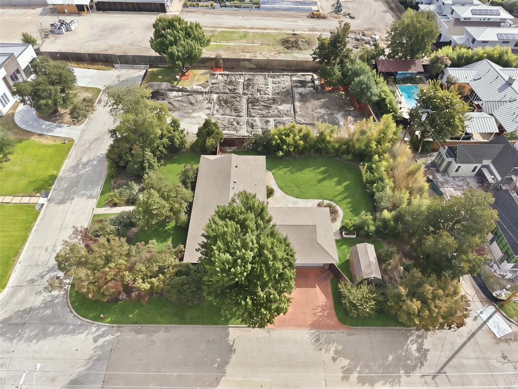 Aerial view of a residential lot featuring a mature tree-lined perimeter, a manicured lawn, a paved driveway, and an exterior storage structure