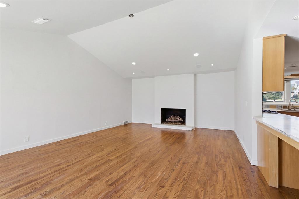 Vaulted ceilings, wood-finish flooring, recessed lighting, and a prominent fireplace with a clean-lined mantel