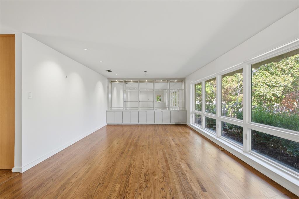 Large living space featuring wood-finish flooring, a wall of floor-to-ceiling windows, recessed lighting, and built-in floor-to-ceiling shelving with glass cabinet fronts