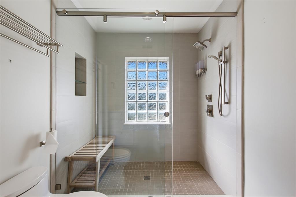 Walk-in shower featuring a glass enclosure with a sliding door, dual shower heads, a built-in recessed niche, and a glass block window