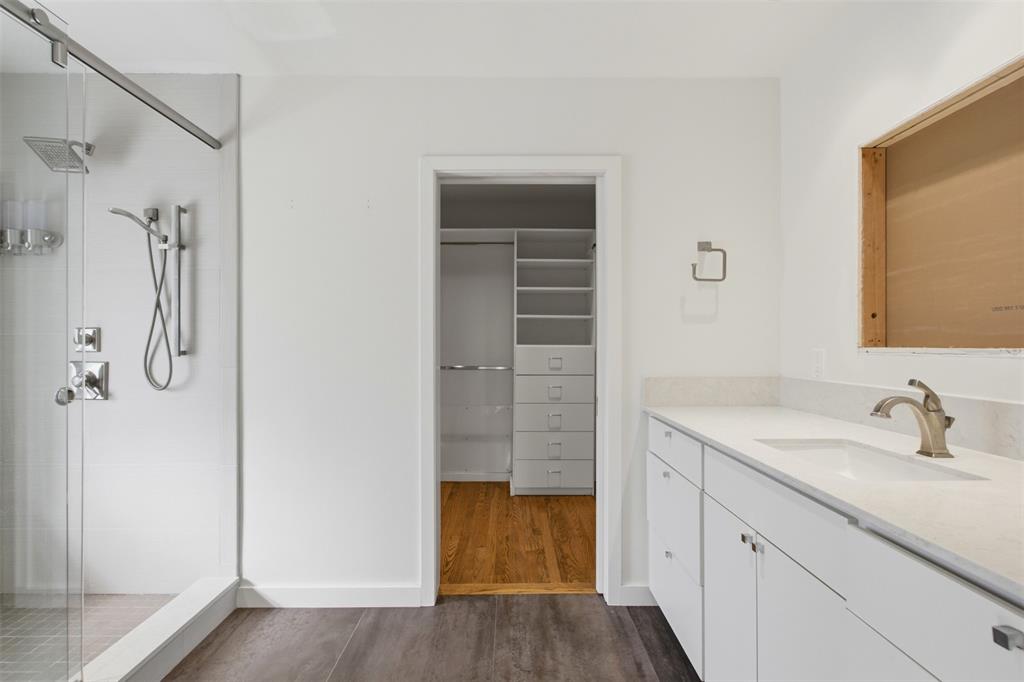 Walk-in shower with glass enclosure and rainfall showerhead, vanity with stone-style countertop and undermount sink, and built-in closet organization system