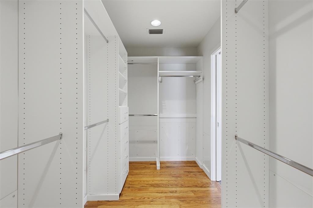 Walk-in closet featuring white built-in shelving, integrated dresser drawers, chrome hanging rods, and wood-finish flooring