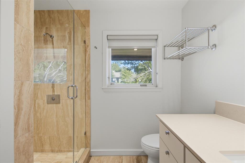 Walk-in shower with stone-tile surround, glass enclosure, polished metal hardware, integrated vanity with composite countertop, and wall-mounted metal shelving