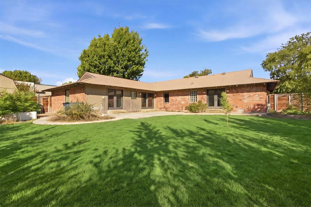 Rear exterior featuring a brick facade, multi-pane French doors, concrete patio, and a manicured lawn