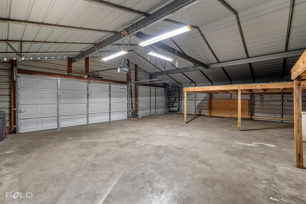Spacious metal-frame structure featuring concrete flooring, multiple overhead garage doors, high-output fluorescent lighting, and elevated wooden platform storage