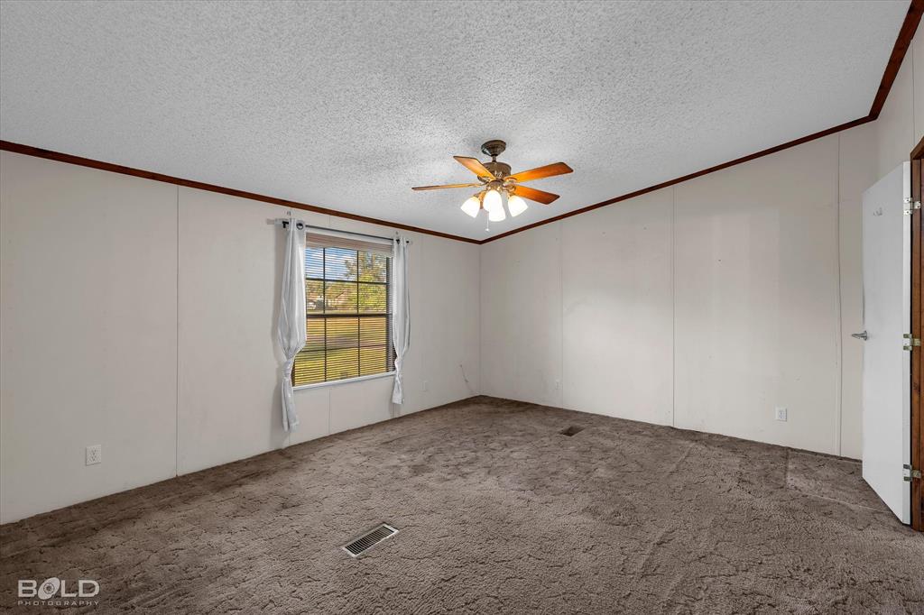 Interior space featuring textured ceilings, dark carpeting, wood-finish crown molding, a central ceiling fan with integrated lighting, and a single-pane window