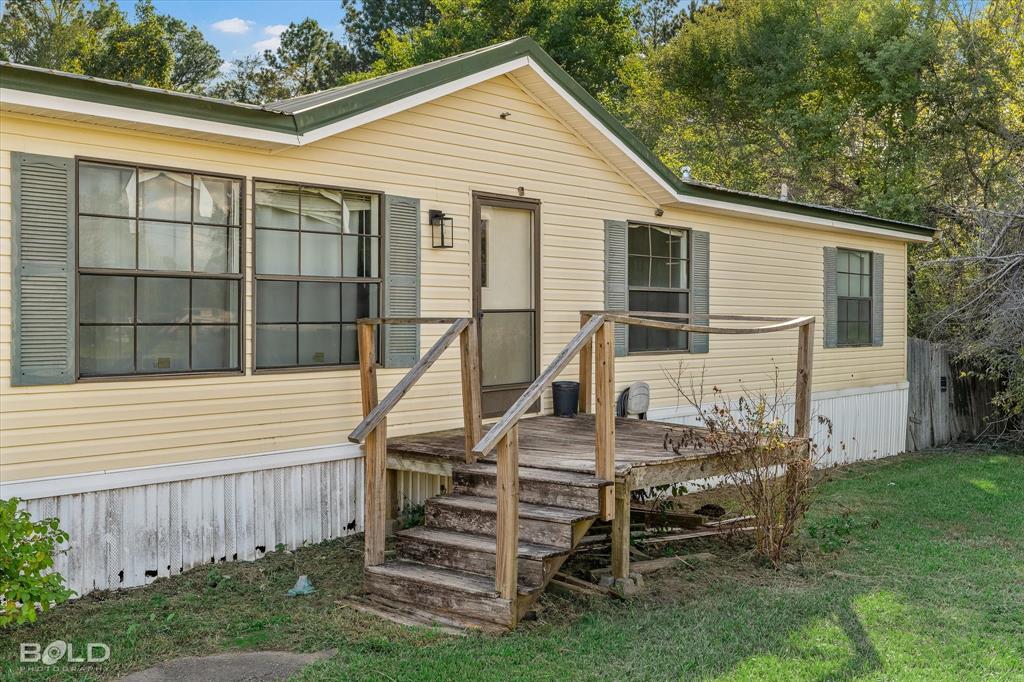 Exterior featuring light-colored horizontal siding, dark-toned shutters, multi-pane windows, and a raised wooden entrance deck with railings