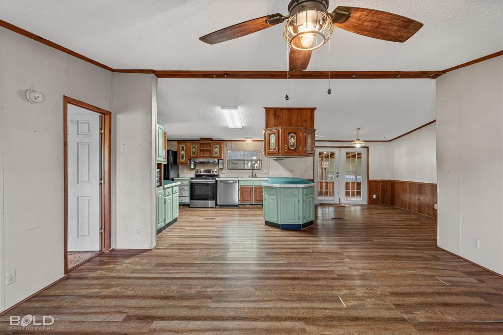 Open-concept interior featuring wood-finish flooring, a central kitchen island, wood-paneled accents, a ceiling fan with integrated lighting, and glass-paneled double doors